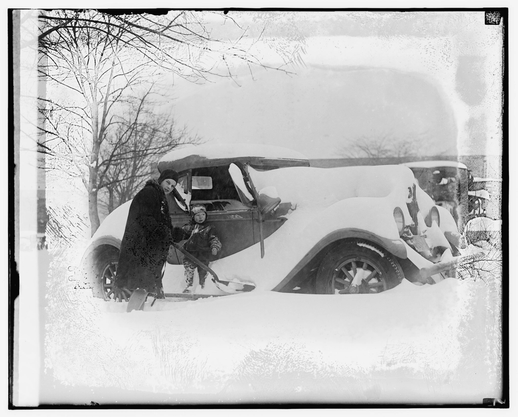 Person clearing automobile covered snow